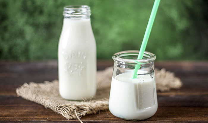 Two glass containers filled with white milk. One container has a green straw. 